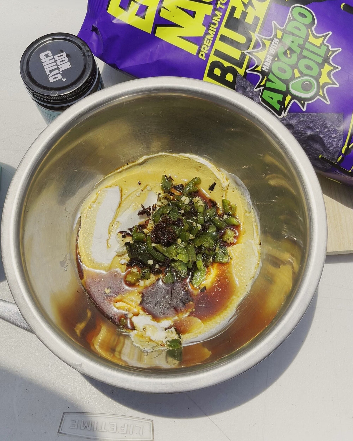 Habanero dip in a bowl, jocoque topped with charred jalapeños and Don Chilio Flamin' Habanero Chili Crisp, next to a bag of El Nacho blue corn chips